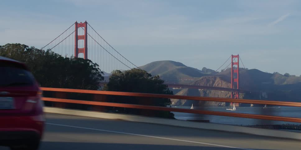 Cars speed by as a large bridge looms in the distance