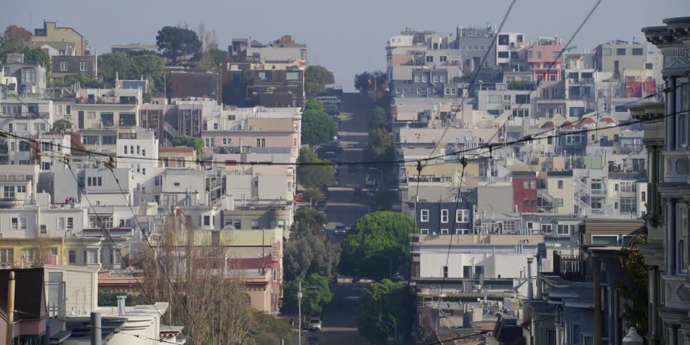 Hilly city street with buildings poles and vehicles