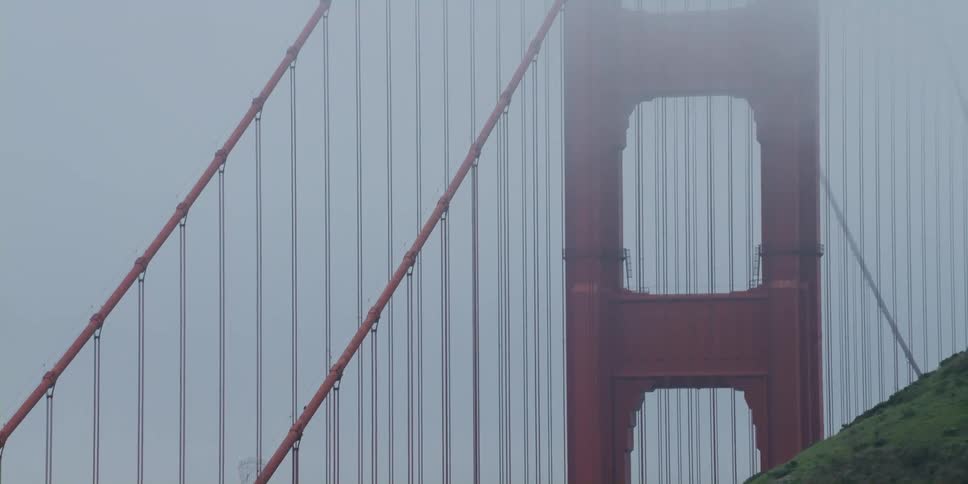 Fog obscures parts of suspension bridge standing near hill