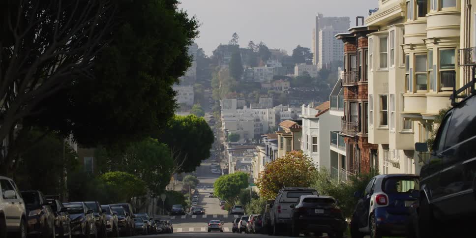 Cars park on street sitting on hill near homes in fog covered city