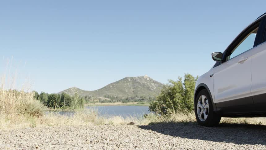 A woman exiting a car after she parks near a lake