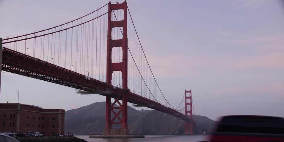 Distant view of suspension bridge with suspension cables on vertical suspenders over river at dusk