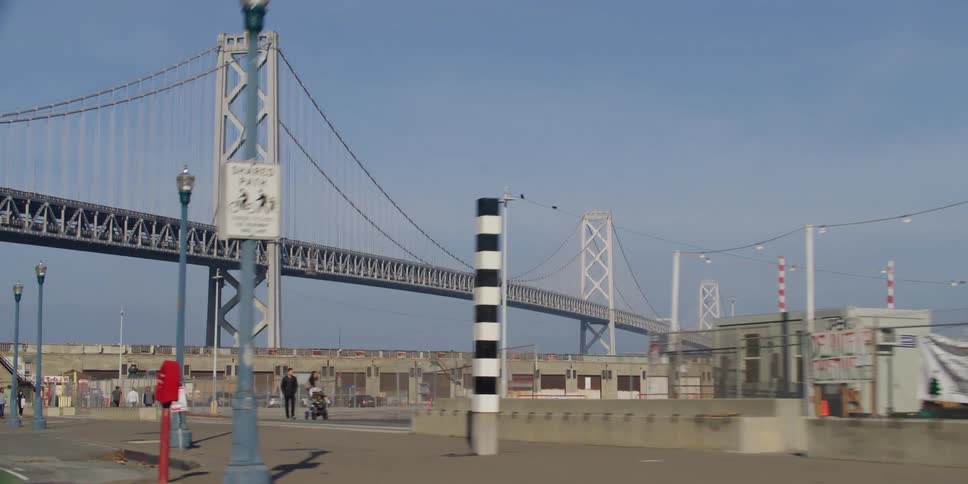 People walk and jog along sidewalk near suspension bridge on foggy day