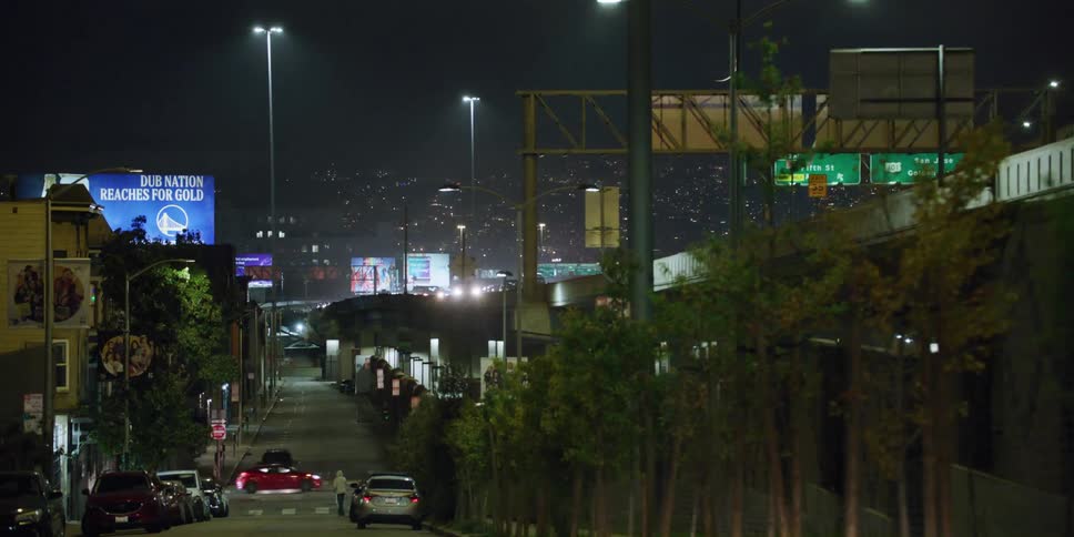 People and traffic pass down a city street that runs alongside a highway