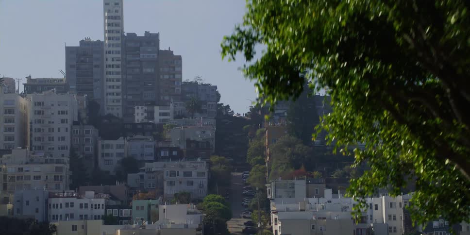 Apartment buildings of varying sizes and heights fill a city neighborhood along a steep hill
