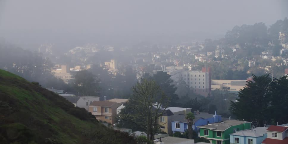 Driving near a small colorful town in the hills under the fog at morning
