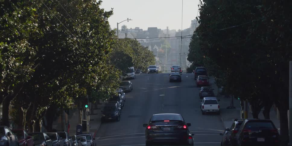 Vehicles drive up and down a hill through a city neighborhood