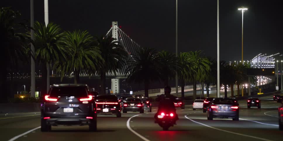 Vehicles driving on the traffic in the highway leading to a suspension bridge at night