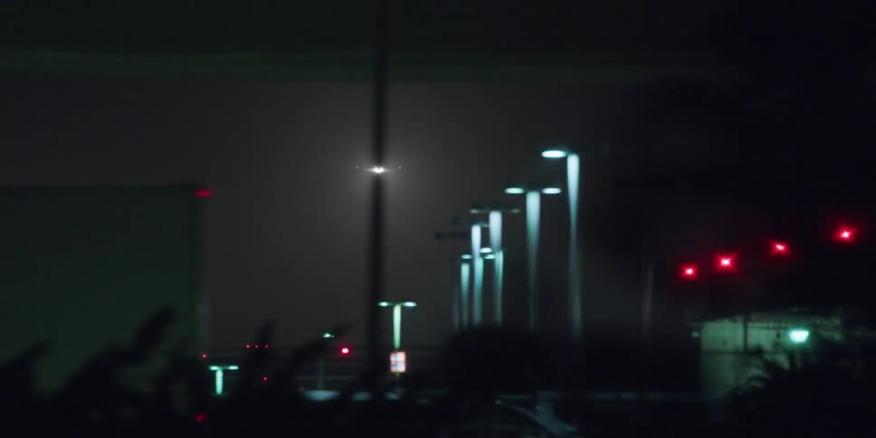 Truck driving past several light poles while a airplane approaches landing
