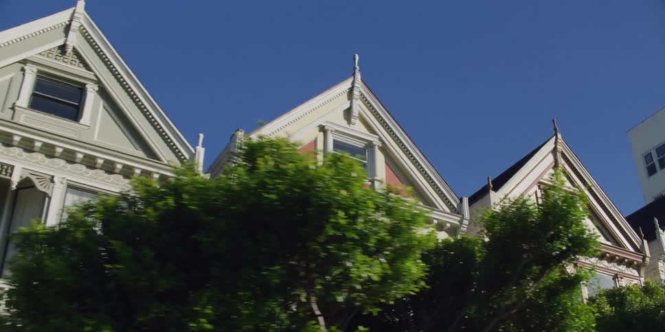 Pedestrians and cars pass tall homes and parked cars