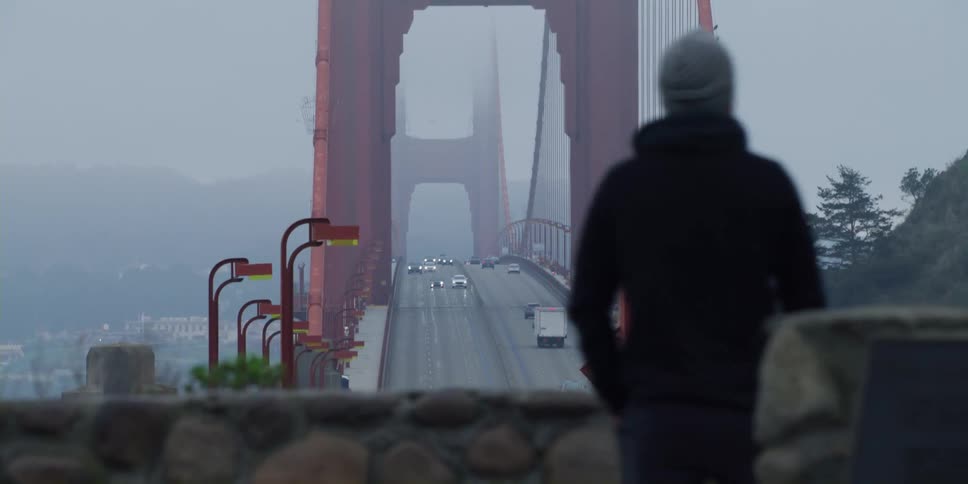 Two men watch from an overpass as traffic drives across the golden gate bridge