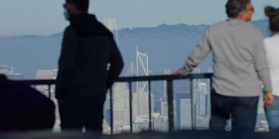 People stand against rail overlooking fog covered city bordered by mountain
