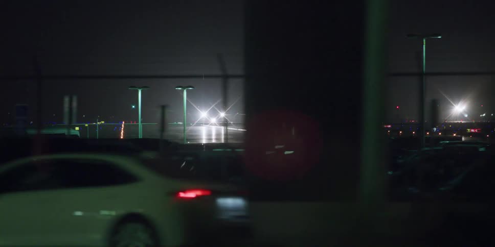Cars travel past an airport with a jet sitting on a runway at night