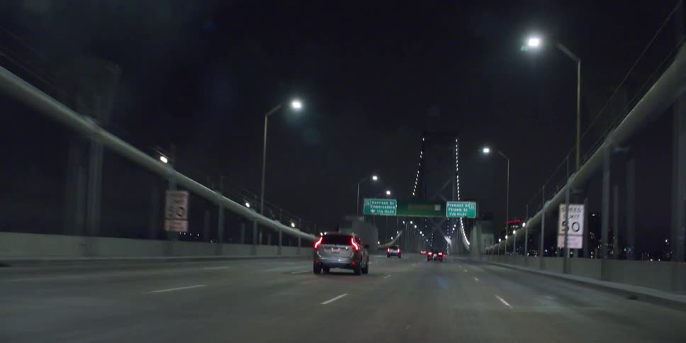 Vehicles speed down a suspension bridge at night