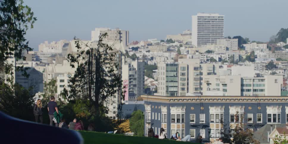 A group of people sit on a hill overlooking downtown