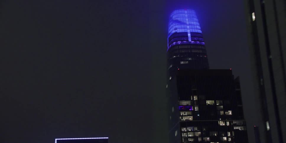 The top of a downtown skyscraper glows blue at night