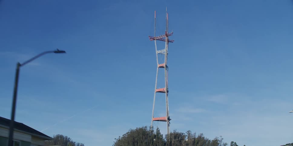 A utility tower stands tall above the trees in a blue sky