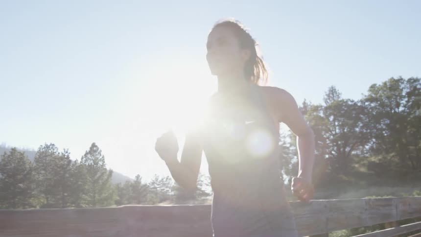 Woman jogging next to a wooden fence at sunset