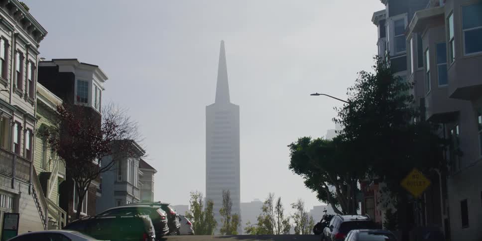 The transamerica pyramid building is visible at the end of a san francisco neighborhood hilly street
