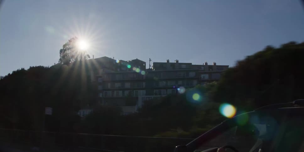 Driver drives car on street passing apartment buildings on a sunny day