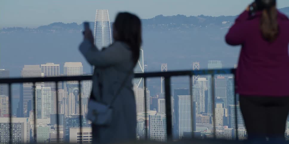 People stand near rail overlooking foggy city taking pictures and viewing skyline