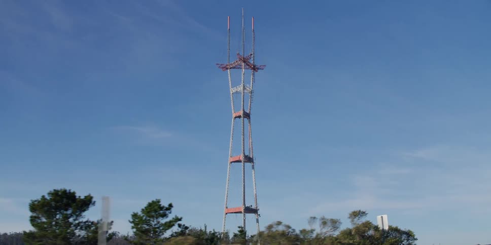 A utility tower stands tall above the trees in a blue sky