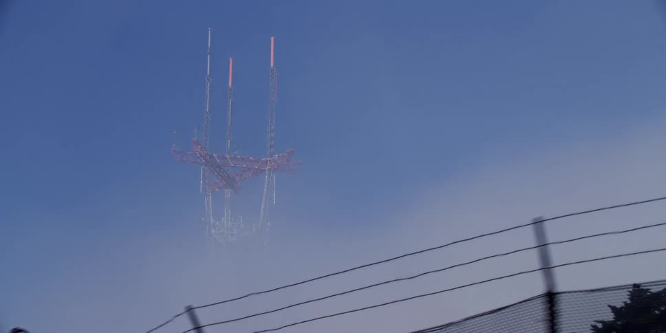 A utility tower stands high among the clouds in the sky