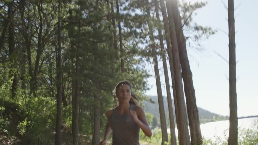 Woman jogging on a trail in a wooded area near a lake