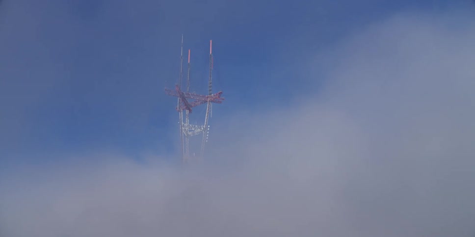 A utility tower stands high among the clouds in a blue sky
