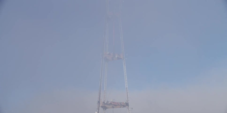 A utility tower stands tall above the trees in the sky