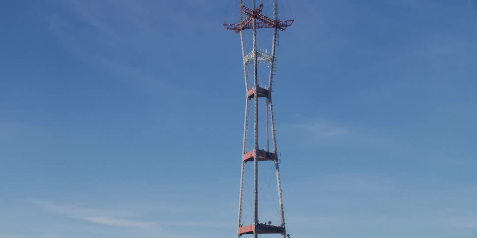 A utility tower stands tall above the trees in a blue sky