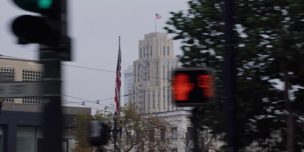 Fog covers highrise topped with american flag in background as pedestrian signal blinks red at an intersection