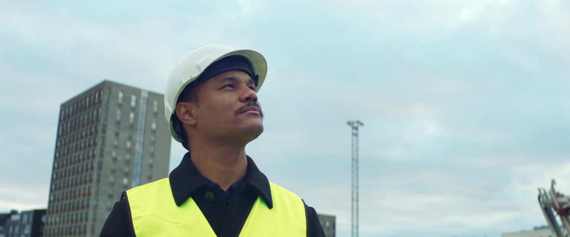 Construction worker reviews clipboard before looking around at urban construction site