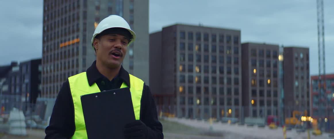 Man wearing a white hardhat and a bright yellow vest supervises a construction site in the city