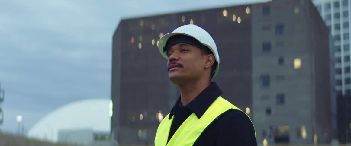 Construction worker weaering a vest and a safety helmet holding a clipboard and talking at a construction site