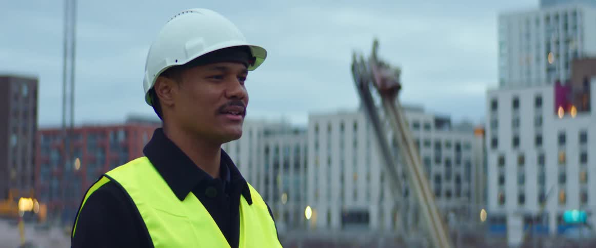 Man wearing a white hardhat and a bright yellow vest supervises a construction site in the city