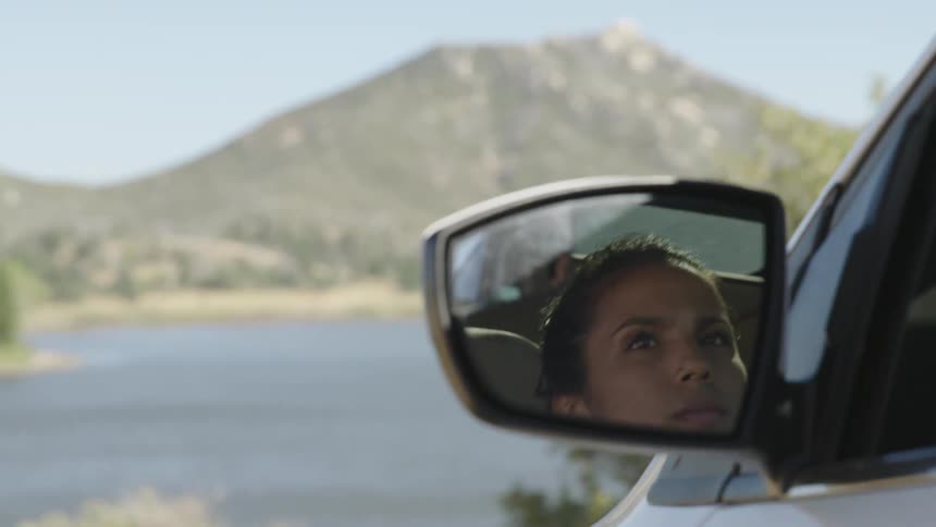 A woman is seen in her driver's side mirror as she parks her vehicle in a natural setting