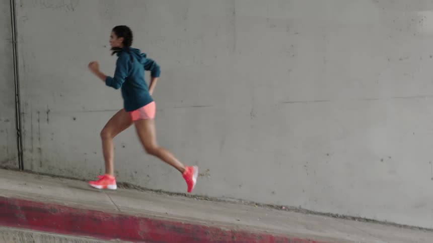 A woman jogs on a sidewalk next to a blank wall