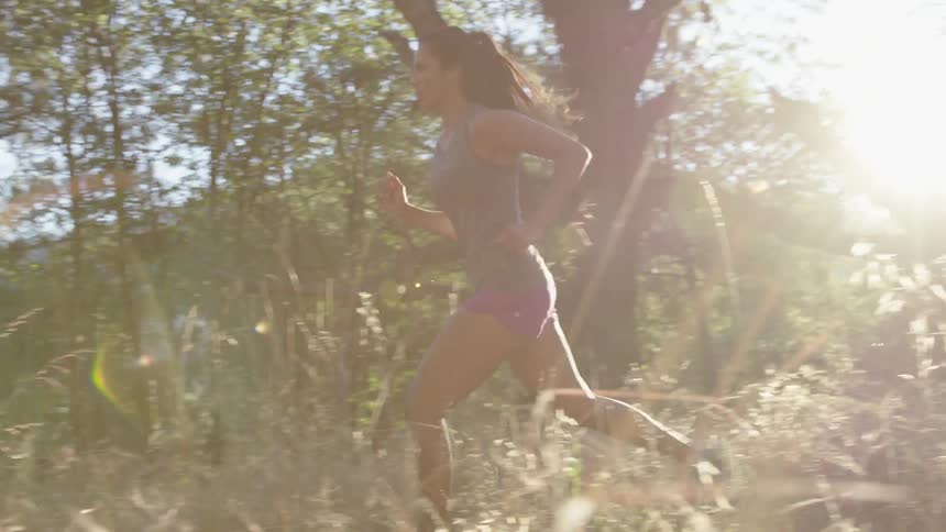 A woman jogs through tall grass and trees