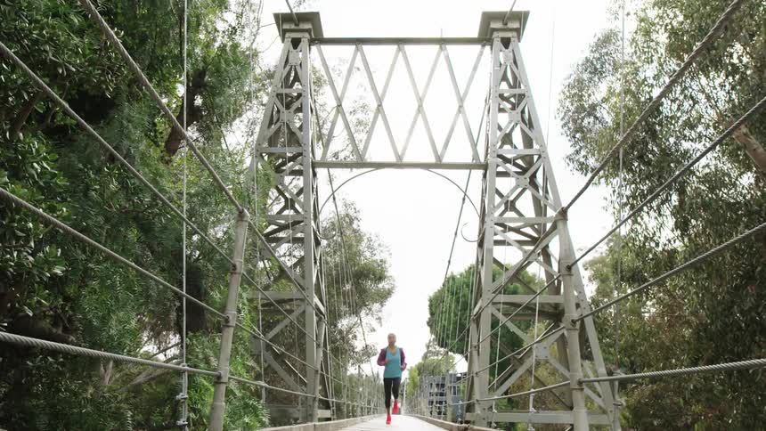 A woman jogging across a suspension bridge