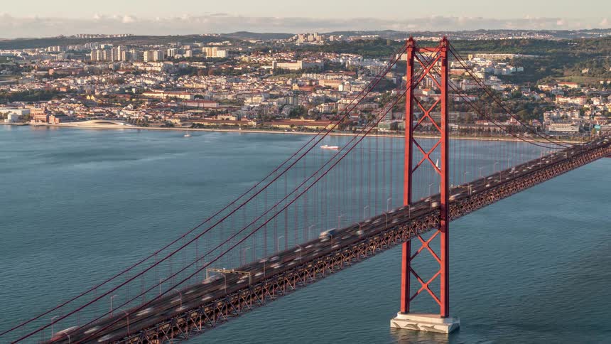 Suspension bridge next to a small city with cars driving in it and boats sailing under it
