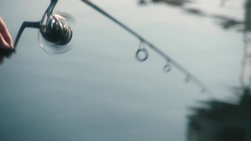 Man fishing on a lake reeling the line at morning