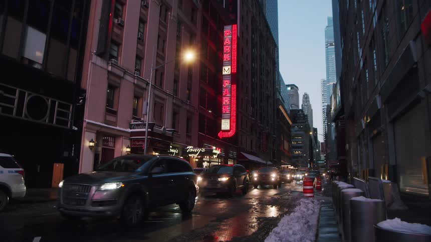 Cars and pedestrians move along city street with snow piled on the edges