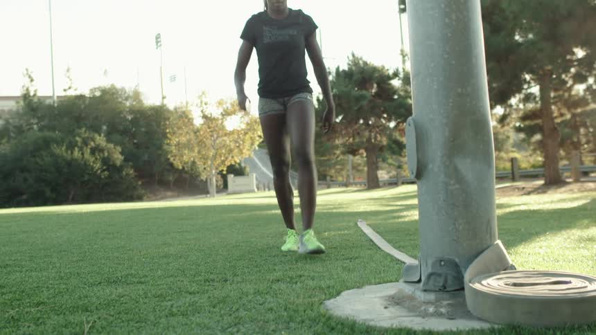 A woman walks over to pole wraps a hose around it
