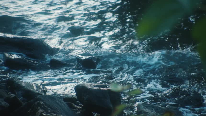 Small waves crashing over the small pebbles and rocks on the coast of a lake at morning