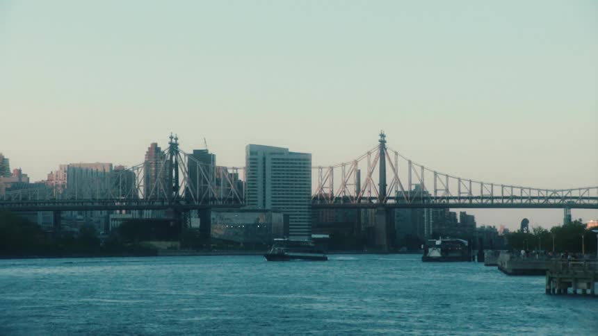 View of a big citys skyline and a suspension bridge over a river with a boat passing by below it