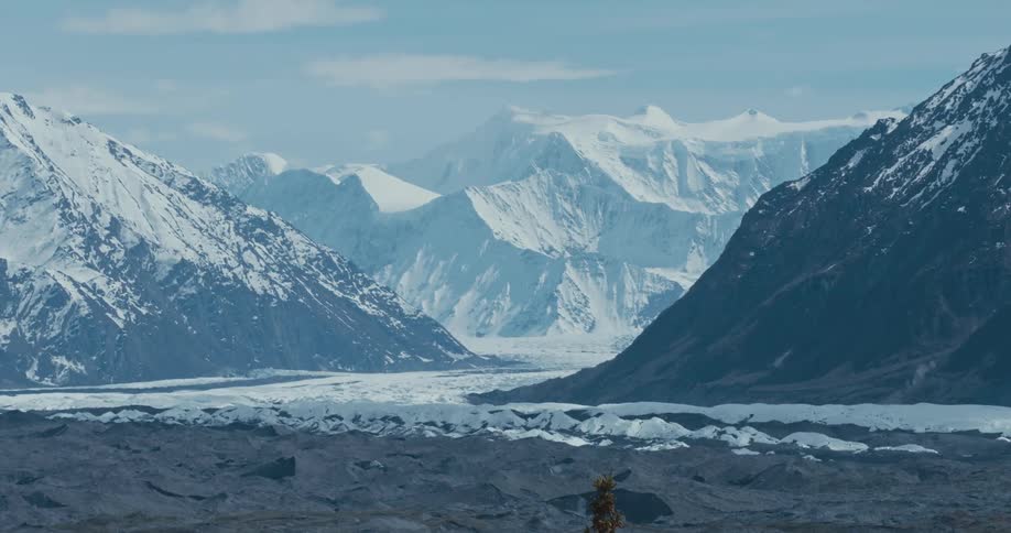 The sun shines on snow covered mountains with peaks high in a cloudy sky