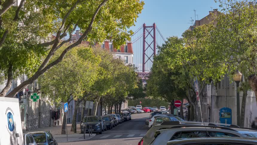 A tree lined street in lisbon with a view of the bridge