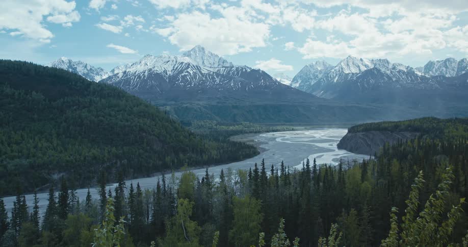 An ice covered river runs through a mountain forest valley with snow covered mountains in the distance
