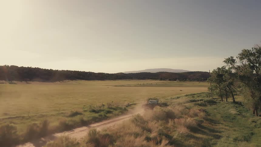 Aerial view of a truck driving on a dirt rural road in the countryside at morning